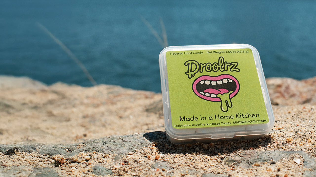 A pack of Droolrz candy sitting on a sandy rock with the ocean in the background